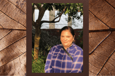 Portrait of Lorena Lopez. She is in front of a tree and window. Lorena has brown hair and eyes and is wearing a purple plaid shirt.